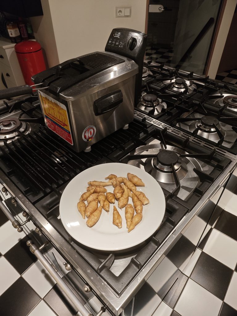 Deep fryer labeled "Tefal" on stovetop

Stainless steel body with black lid and handle

Crosman brand visible with "10" rating label

White plate with small, tuberous vegetables, likely Jerusalem artichokes (Helianthus tuberosus)

Black and white checkered tile floor

Red cylindrical fire extinguisher in the background