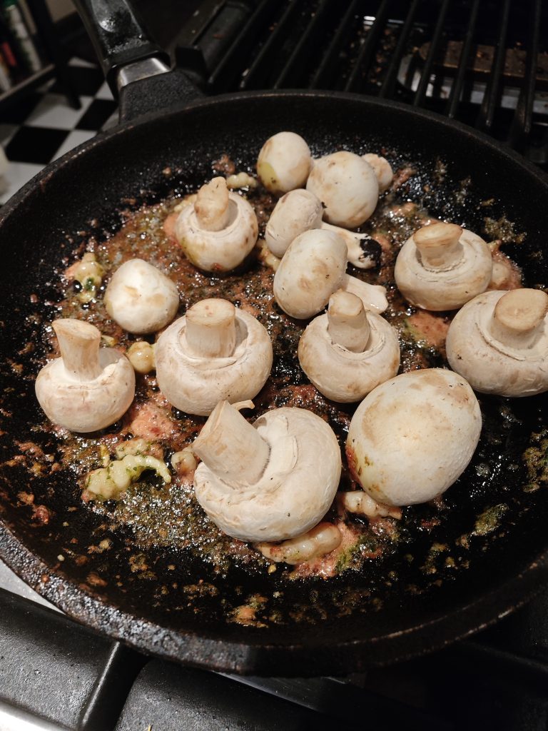 Whole mushrooms being sautéed in a cast iron skillet with garlic and herbs.
